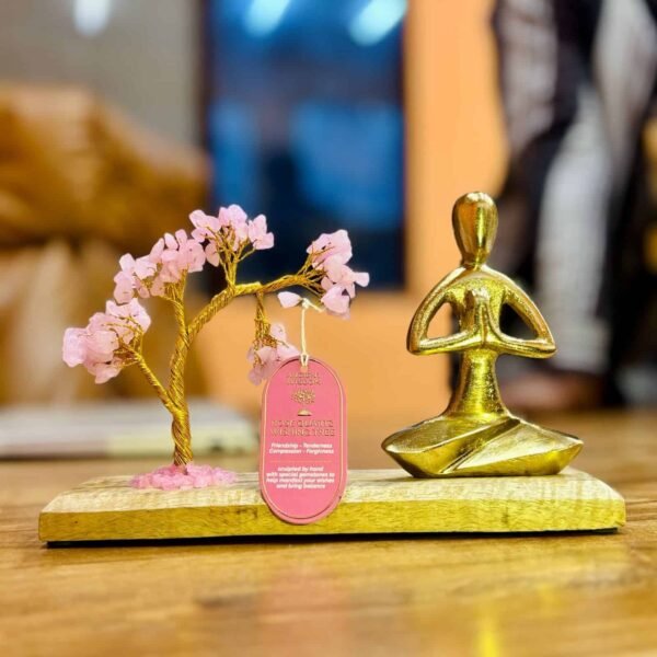 Pink quartz wishing tree with a golden meditation figurine on a wooden base, representing friendship, tenderness, compassion, and forgiveness, available at Sunshine Gifts.