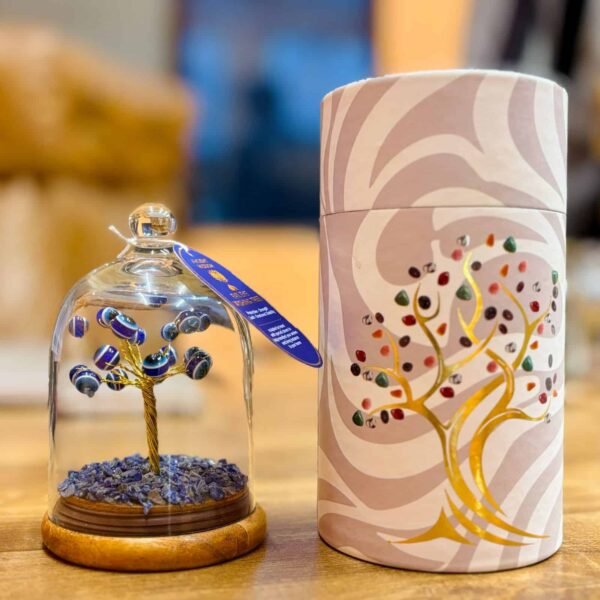 Colourful glass flower tree inside a glass cloche with a wooden base, decorated with blue and white beads, next to an elegant cylindrical gift box with a floral and swirl design.