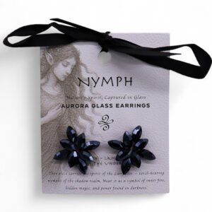 Shiny black flower-shaped Aurora glass earrings with gemstone-like facets, displayed on a pastel pink card with fantasy artwork. Perfect for nature-inspired or mystical jewellery lovers.