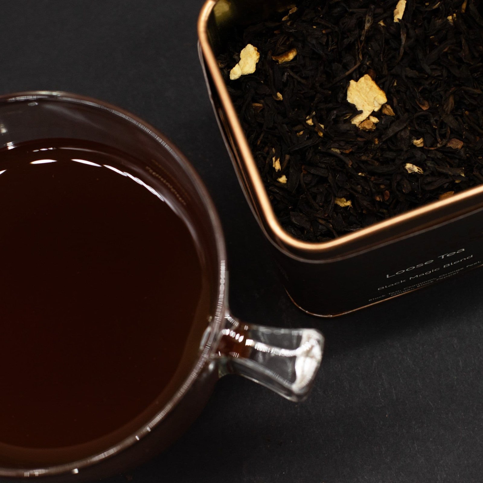 Loose leaf black tea in a glass cup with a metal tin of tea leaves.