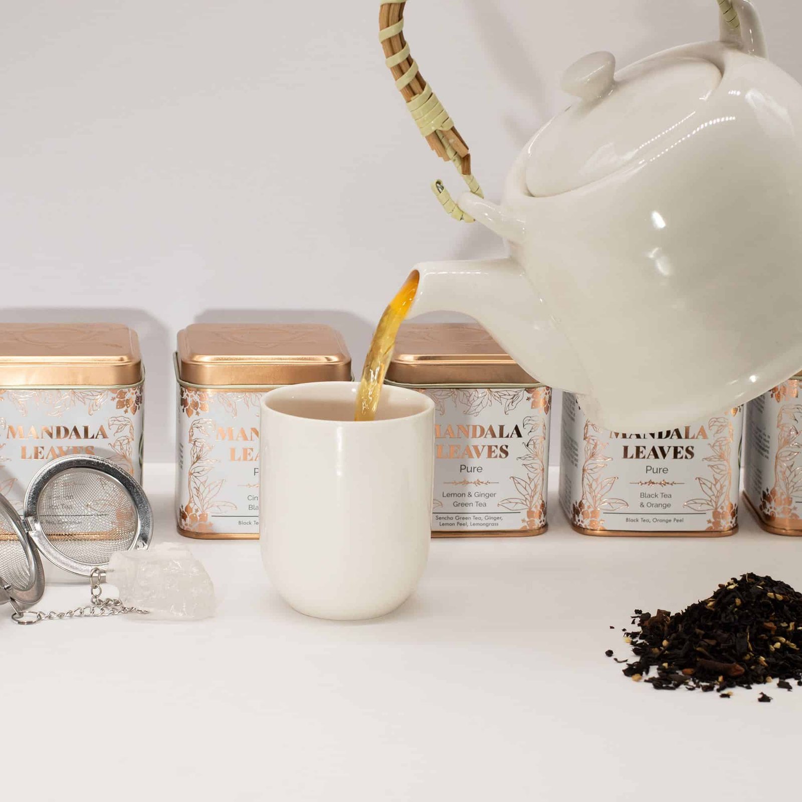 White teapot pouring hot tea into a mug with Mandala Leaves tea tins in the background, showcasing a relaxing tea experience.