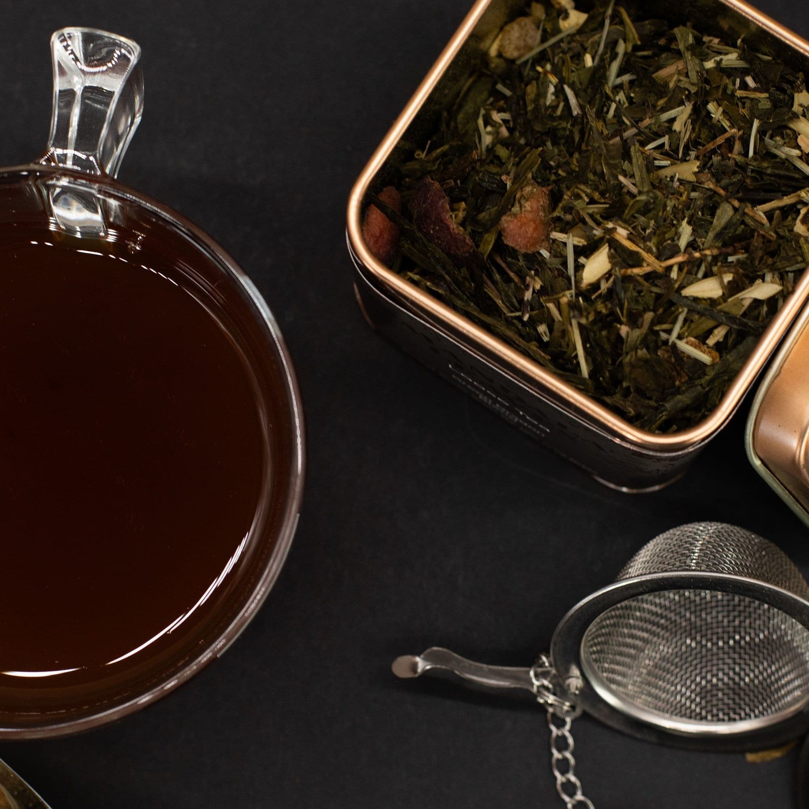 Herbal tea in a glass cup with loose dried herbs and an infuser on a black background, showcasing natural wellness products.