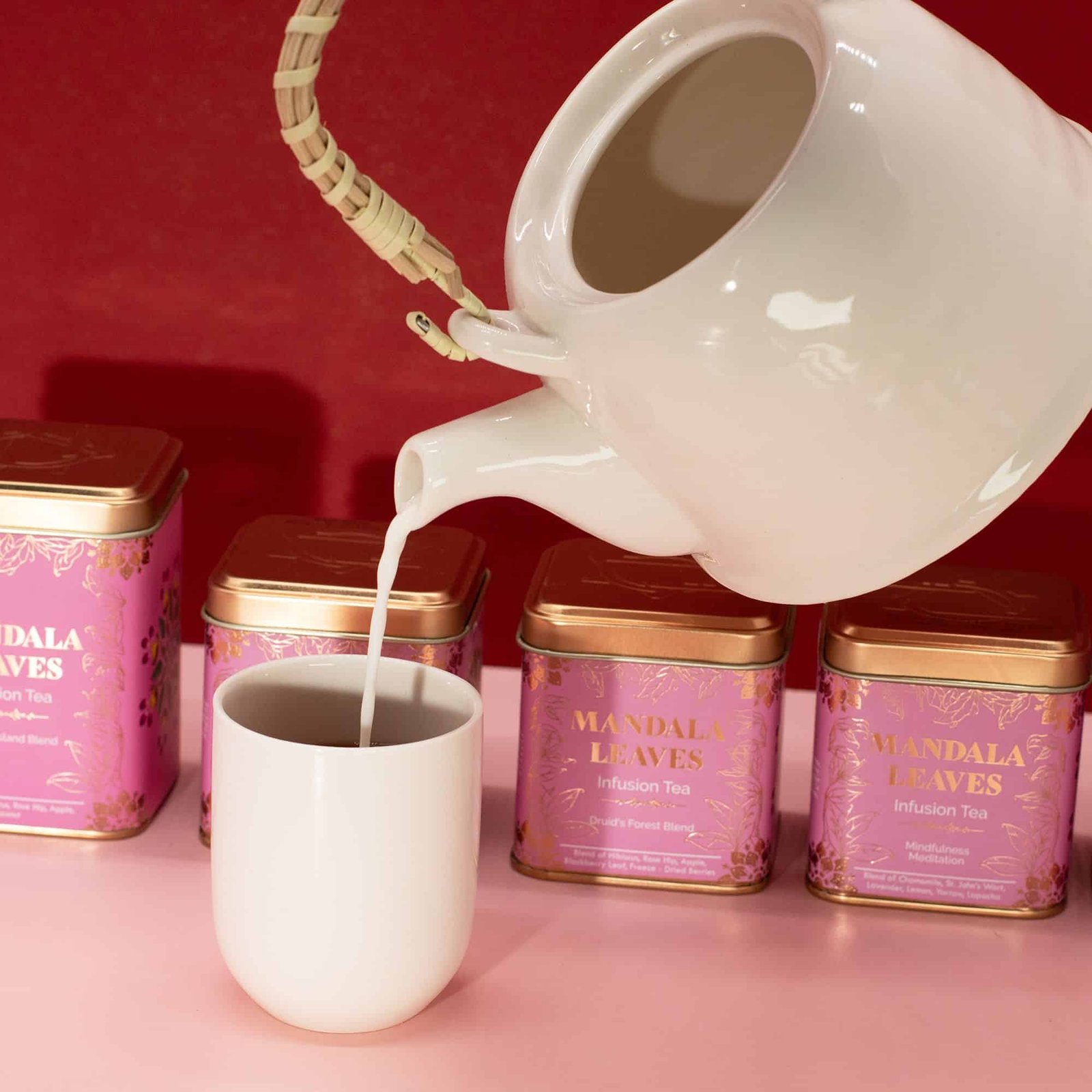 Elegant white mug being filled with hot tea from a white teapot, with Mandala Leaves infusion tea tins in the background, showcasing a calming tea-drinking scene.