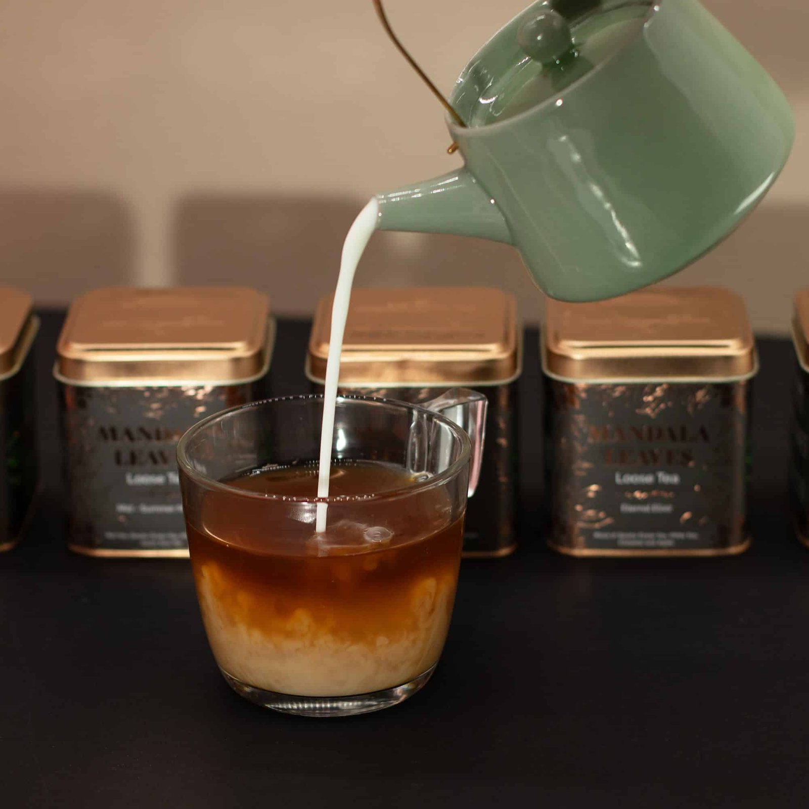Pouring fresh milk into a cup of tea with loose leaf tea tins in the background, showcasing a relaxing tea preparation scene.