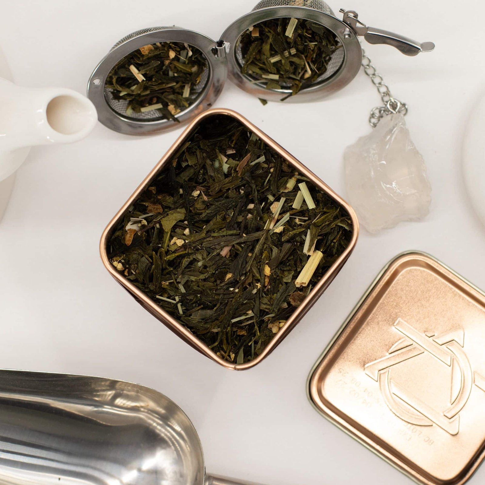 Loose leaf herbal tea in a decorative tin with a glass teapot and crystal on a white background, perfect for tea lovers and gift-giving occasions.