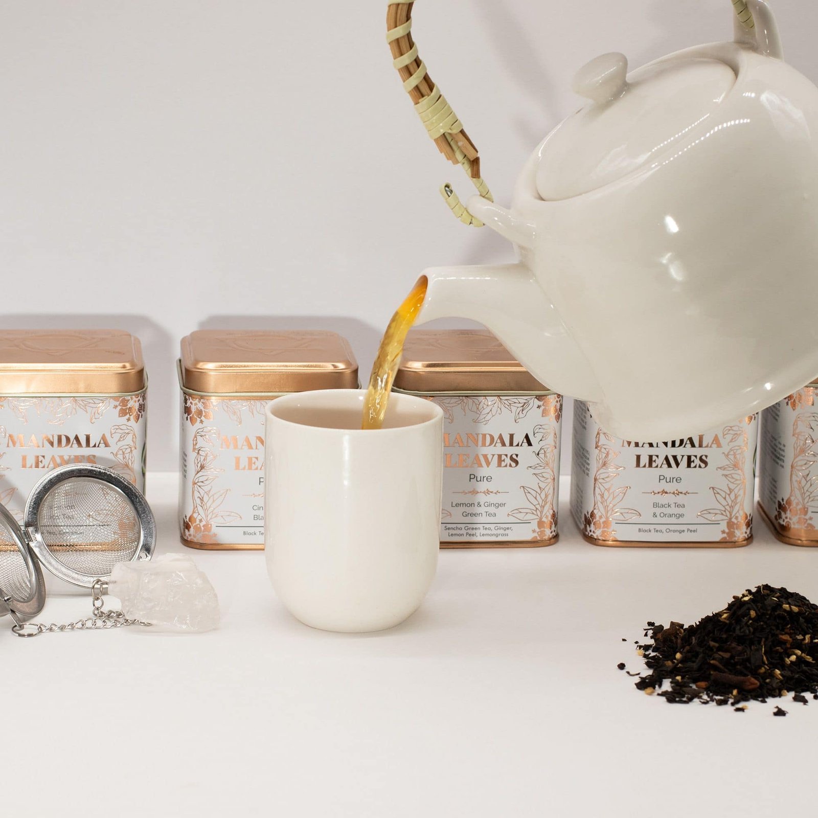 White teapot pouring Mandla Leaves herbal tea into a cup, with Mandla Leaves tea tins in the background, showcasing a relaxing tea experience.